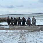 Group of hunters with a row of ducks on a log at wintertime