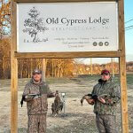 two hunters below Old Cypress Lodge sign with ducks