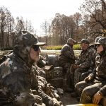 people sitting in a boat wearing camo